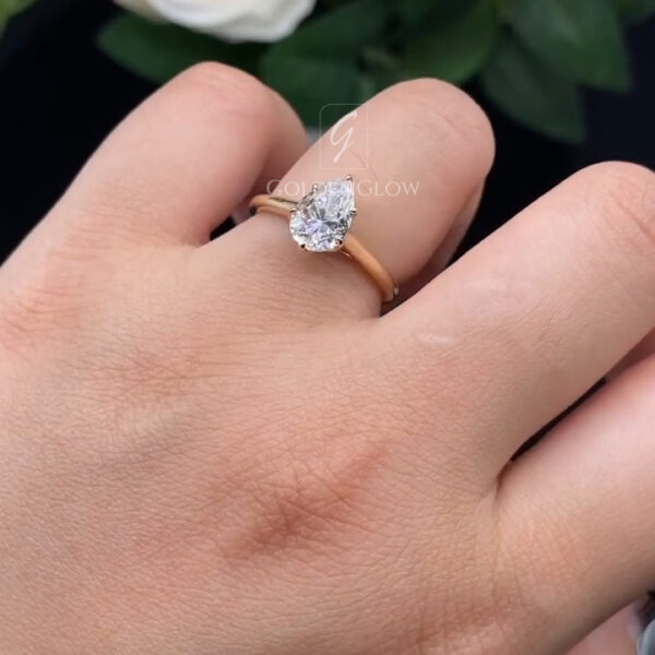 Pear-cut clear lab-grown diamond or moissanite solitaire ring worn on the hand, set in a slim yellow gold band. Soft indoor lighting highlights the teardrop shape and clean, minimal design.