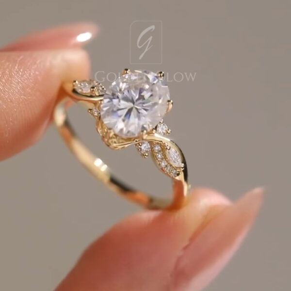 Macro shot focusing on the round brilliant gemstone and prong setting of a yellow gold ring. The intricate metalwork and pavé diamond accents along the band are clearly visible, showcasing sparkle, clarity, and the elegant design elements of this handcrafted engagement ring.