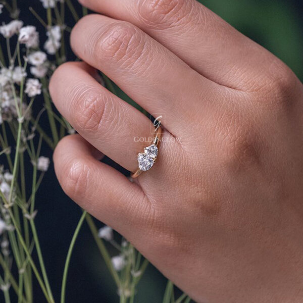 Toi et moi diamond ring featuring two heart-shaped brilliant diamonds set side by side on a slim yellow gold band. The twin stones sparkle under studio lighting, held delicately with precision tools, highlighting fine craftsmanship, symmetry, and modern romantic jewelry design against a soft neutral background, Proposal Ring, Promise Ring, Engagement Ring For Women