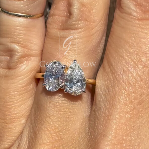 Lifestyle image of a yellow gold toi et moi ring worn on the finger, displaying the elegant pairing of oval and pear diamonds for a modern engagement ring look.