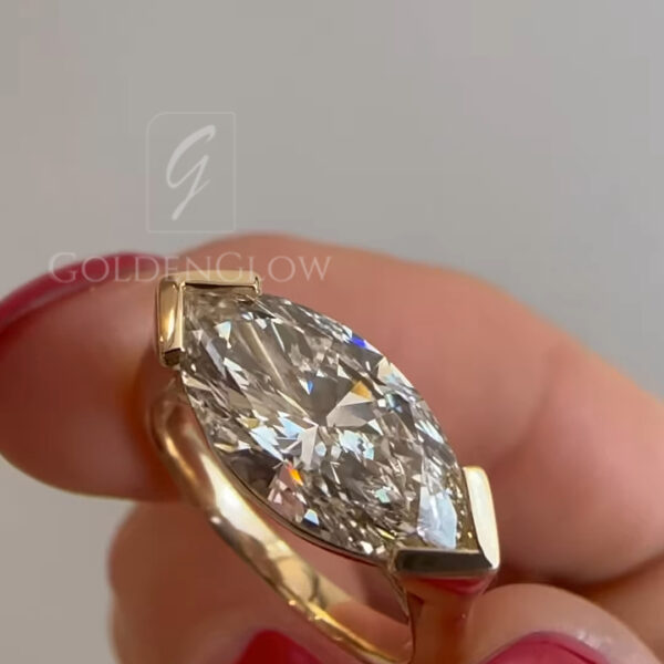Close-up detail of a marquise diamond ring in yellow gold, focused on the elongated center stone and sleek band profile. The diamond’s pointed ends and brilliant facets are clearly visible, framed by a refined gold setting that enhances durability and style. The neutral background keeps attention on the fine jewelry craftsmanship, showcasing a contemporary marquise-cut engagement ring with clean lines and elegant design.