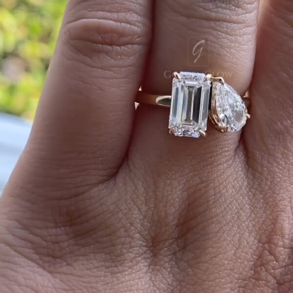Close-up of a hand wearing an asymmetrical toi et moi ring with two clear stones in different shapes. The emerald-cut and pear-cut stones reflect daylight, emphasizing contrast, balance, and contemporary elegance.
