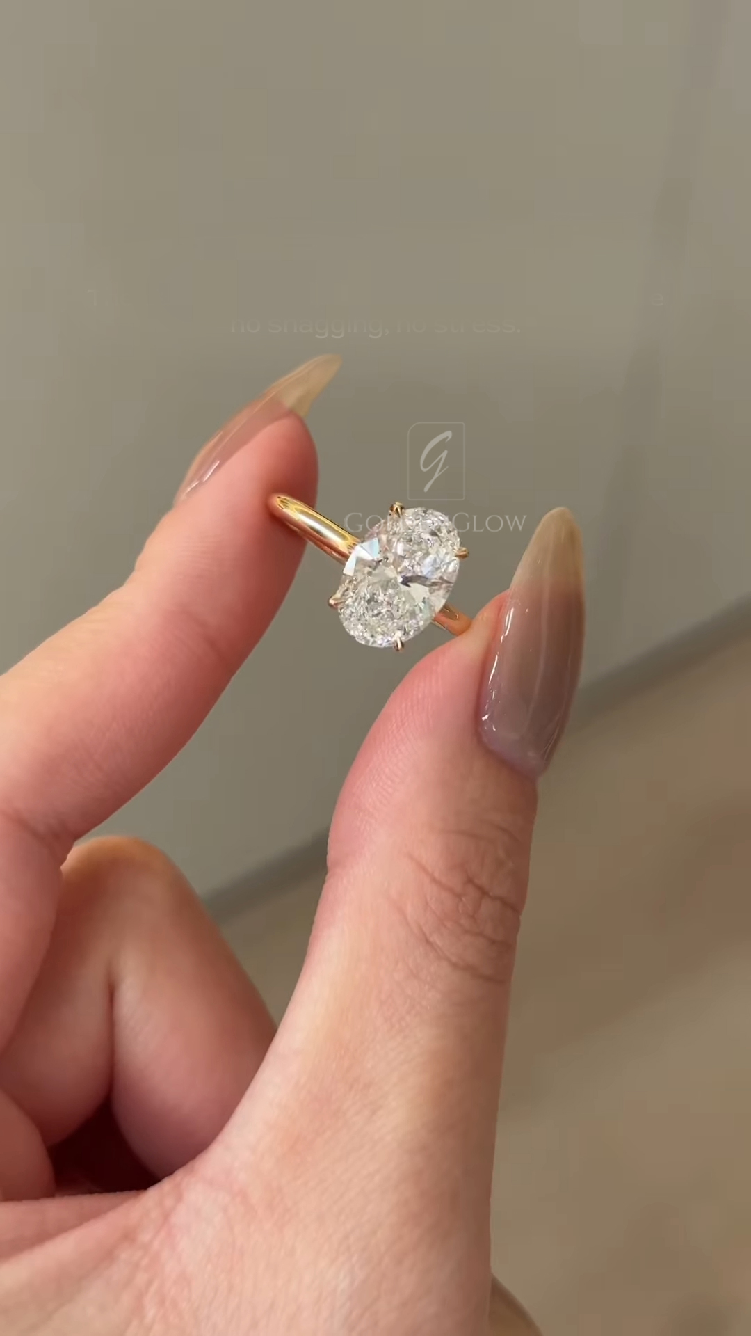 Close-up side view of an oval-cut white diamond engagement ring on a hand, set in yellow gold. The solitaire diamond is shown from a low angle highlighting the slim band, prong setting, and sparkle under natural light.