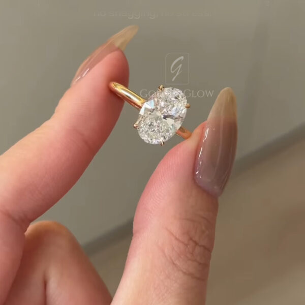 Angled close-up of the oval-cut diamond engagement ring focusing on the stone’s height and sparkle. The yellow gold band and prongs are clearly visible against a soft neutral background.