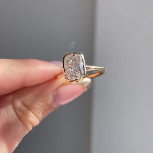 Angled view of a bezel-set engagement ring showcasing an elongated cushion lab grown diamond framed by a refined yellow gold bezel. The sleek band enhances the stone’s shape while maintaining a minimalist aesthetic. Designed for everyday comfort and contemporary style, this ring is also offered with a moissanite diamond option, providing a radiant, eco-friendly choice with diamond-like sparkle and durability.