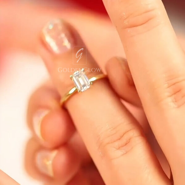 A top-down view of the ring worn on a hand, showing real-world scale. The emerald-cut diamond or Moissanite elongates the finger elegantly. The step facets catch the ambient light, creating a soft, sophisticated glow. The white gold band blends with the skin tone, enhancing the "floating stone" illusion. This image is perfect for demonstrating the finger coverage and the timeless, understated appeal of a simple emerald-cut solitaire.