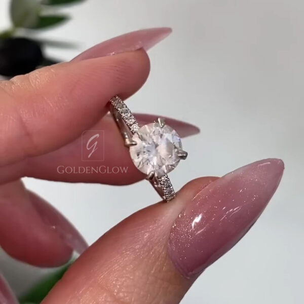 A breathtaking top-down close-up of the ring, focusing entirely on the brilliance of the oval center stone and its surrounding halo. The diamond or Moissanite features a "crushed ice" facet pattern, reflecting light in a dazzling array of sparkles. The seamless halo of smaller diamonds increases the visual footprint of the ring, making the center gem appear massive. This shot emphasizes the colorless quality of the stone and the perfect symmetry of the oval shape, ideal for a statement engagement piece.