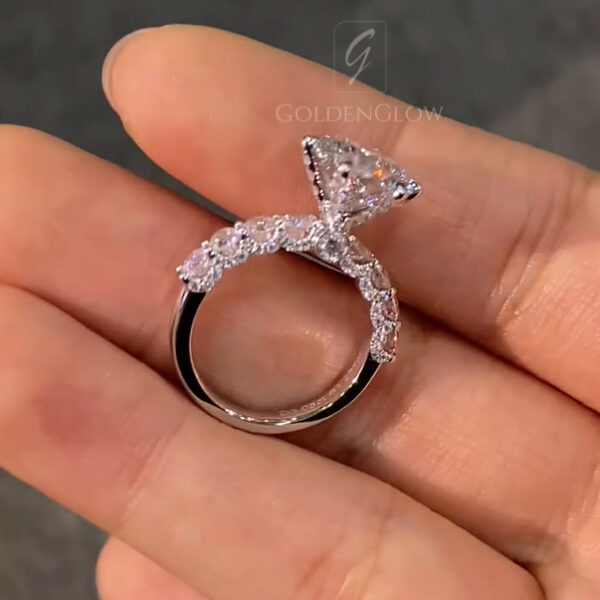 Close-up back profile of a round engagement ring displayed on the palm, showcasing a diamond elevated above a pavé-accented band in polished white metal. Light passes through the center stone, enhancing clarity and sparkle. This angle helps illustrate differences buyers consider between a lab grown diamond and a moissanite diamond, including light dispersion, brilliance pattern, and overall visual balance.