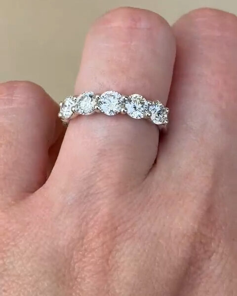 Side profile of a round stone eternity band resting on a finger, showing detailed prong settings and uniform stone height across the band. The polished white metal reflects light subtly while each round stone displays crisp facets. This image helps illustrate craftsmanship differences between a lab grown diamond and a moissanite diamond, emphasizing durability, sparkle, and classic elegance in an eternity wedding band design.