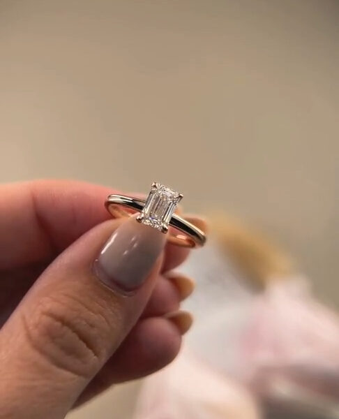 Side profile of an eternity ring held gently between thumb and forefinger, revealing the prong setting and precise alignment of each gemstone along the band. The lighting accentuates sparkle and depth while keeping the background neutral and unobtrusive. This image is useful for visualizing differences between a lab grown diamond and moissanite diamond, focusing on setting height, stone placement, and reflective quality.