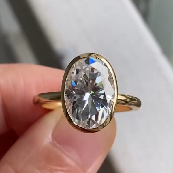 Side-angle view of an oval bezel engagement ring featuring a lab grown diamond secured in a smooth yellow gold setting. The elevated profile reveals the pavilion and under-gallery, allowing light to pass through the stone. This refined craftsmanship emphasizes durability and brilliance, offering a timeless alternative often evaluated alongside a moissanite diamond for ethical and sustainable fine jewelry choices.