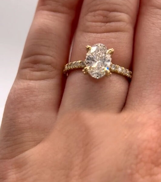 Macro image of a diamond oval solitaire ring worn on the hand, revealing scale, proportion, and brilliance in natural lighting. The yellow gold pavé band adds warmth and texture, while the center stone reflects crisp flashes of light. Created to visually compare wearability and sparkle differences between a lab grown diamond and a moissanite diamond in real-life conditions.