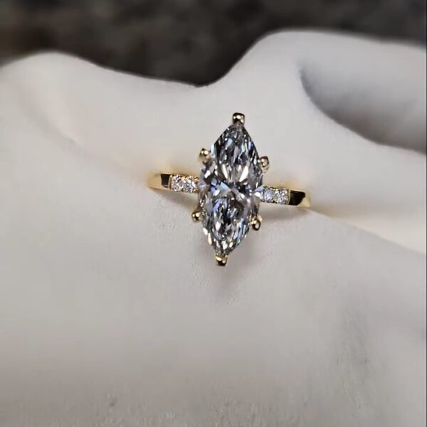Close-up front view of a marquise-cut lab-created diamond or moissanite engagement ring in yellow gold. The vertically set center stone appears symmetrical and elongated, creating a flattering finger-lengthening effect. Fine prongs secure the stone while maintaining a light, airy appearance. The slim band with subtle side stones adds balance and brilliance, making this ring ideal for a modern, sophisticated aesthetic.