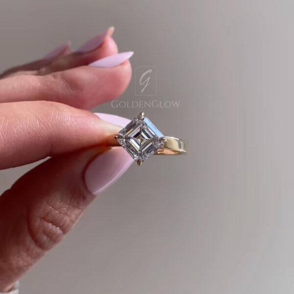 A sophisticated angled view of a square Asscher-cut solitaire engagement ring. The centerpiece is a pristine lab grown diamond or Moissanite, held securely by four claw prongs in a polished 18k yellow gold setting. The step-cut facets create a "hall of mirrors" effect, drawing the eye deep into the stone. The band is smooth and substantial, tapering slightly towards the head. This image captures the geometric elegance and vintage appeal of the square cut, perfect for a bride who values Art Deco style.