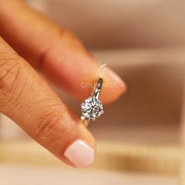 A classic side-profile view of a round brilliant-cut solitaire engagement ring. The 18k white gold or platinum band is polished to a mirror finish, tapering slightly as it reaches the head. The lab grown diamond or Moissanite is held in a secure four-prong basket setting, elevated to allow light to pass through the pavilion. This profile shot emphasizes the timeless simplicity of the design, showcasing the stone’s height and the clean, architectural lines that make it a universal symbol of elegance.