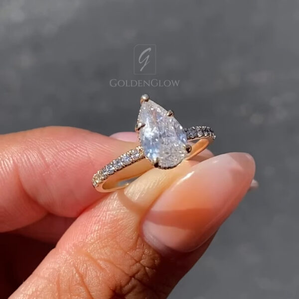 Side profile image of a pear-cut engagement ring showcasing the elevated prong setting and pavé diamond band. The diamond centerpiece reflects light beautifully, allowing maximum brilliance and sparkle from every angle. Crafted in warm rose gold, this solitaire engagement ring blends classic design with modern refinement. It is also available with a moissanite diamond, providing an eco-conscious choice with diamond-like brilliance and durability.