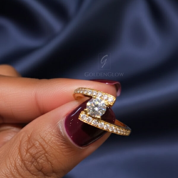 Close-up image of a modern open-band engagement ring held between fingers with deep burgundy nail polish, set against soft navy satin fabric. The ring features a round center stone secured in a sculptural tension-style setting, with pavé stones along the curved band. The center stone may be a lab grown diamond or a moissanite diamond, reflecting bright white sparkle and fire under soft lighting, emphasizing fine craftsmanship and elegant contemporary design.