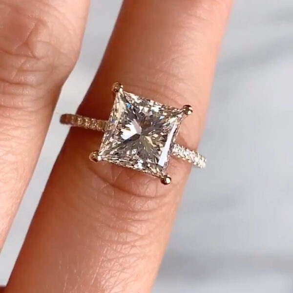 Detailed macro shot focusing on the crown and prongs of a square lab grown diamond engagement ring. The camera captures the sharp facet junctions and reflective surface as the ring rests on a finger. The pavé band curves gently beneath the setting, producing light play often compared to a moissanite diamond, while showcasing the clarity, structure, and balanced brilliance unique to a diamond.