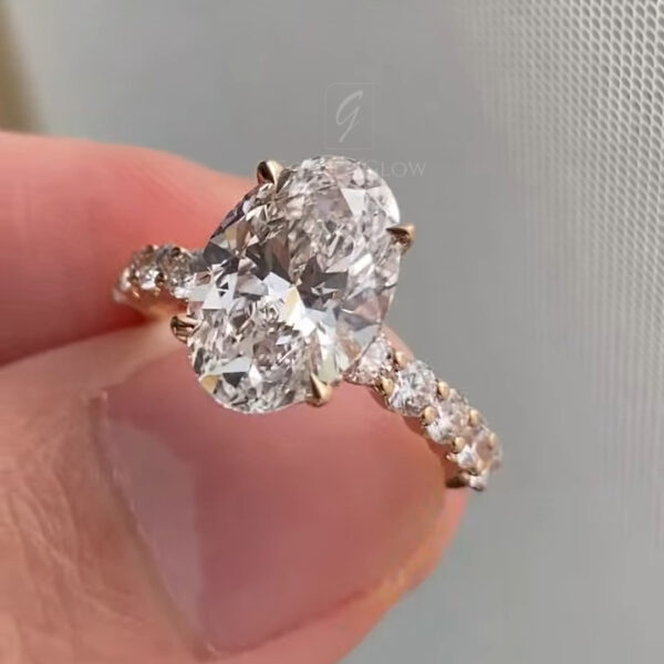 Macro photograph of a Moissanite diamond engagement ring shown from the side, focusing on the pavé-set yellow gold band and elevated oval center stone. The Moissanite diamond exhibits crisp facets and balanced proportions, while the gallery and prongs are clearly defined. The ring is held by a hand with neutral nails, and the soft background keeps attention on ethical luxury and fine jewelry craftsmanship.