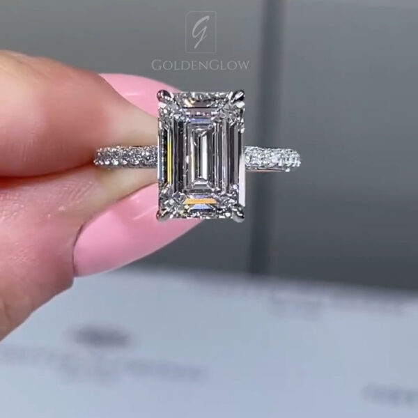 Close-up side profile of a luxury engagement ring featuring an emerald-cut center stone set in a white metal band with pavé diamonds. The elevated basket and prong structure highlight the stone’s depth and clean step facets. This detailed view showcases craftsmanship and sparkle, ideal for comparing a lab grown diamond versus a moissanite diamond in terms of brilliance, fire, and setting height on a modern fine jewelry ring.