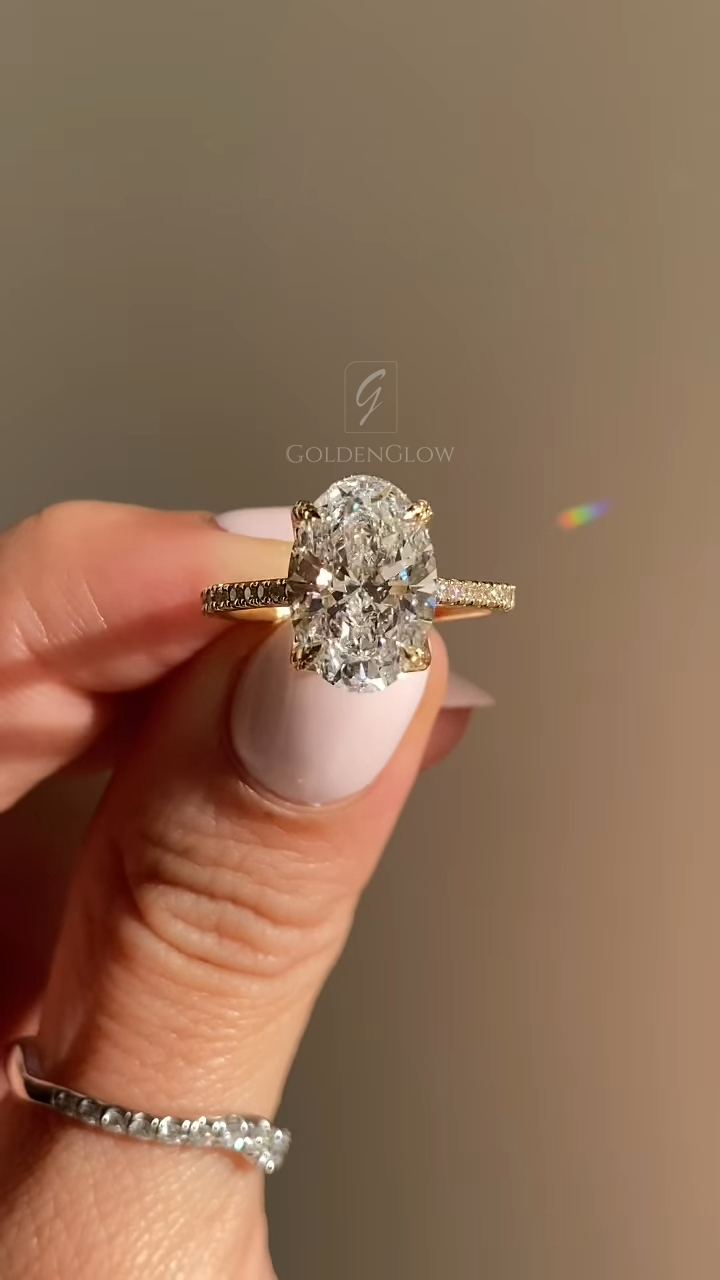 A stunning profile view of a vintage-inspired engagement ring. The 18k yellow gold band features intricate scroll engraving on the side walls, adding heirloom charm. The center stone, a massive oval-cut lab grown diamond or Moissanite, sits atop a hidden halo of micro-pavé stones. This angle highlights the craftsmanship of the hand-engraved details and the brilliant fire of the sustainable gemstone, blending antique aesthetics with modern ethical luxury.