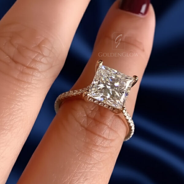 Macro shot of a square engagement ring highlighting the center stone’s internal reflections and the delicate pavé diamonds along the band. The gemstone sparkles vividly as light moves across its surface, while the polished gold setting provides a smooth, elegant frame. The deep blue background enhances contrast and luxury appeal. Ideal for showcasing fine jewelry options such as a lab grown diamond or moissanite diamond engagement ring.