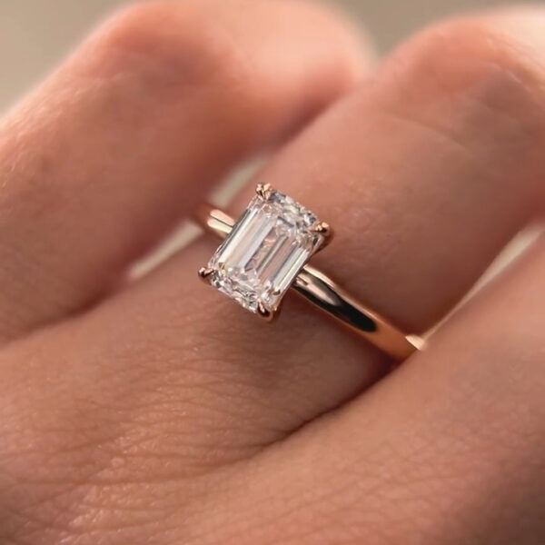 Close-up view of a hand holding a delicate eternity band between the fingers, showcasing a continuous row of sparkling stones set in polished white metal. The ring is photographed against a soft gray background, highlighting the brilliance and symmetry of each stone. Ideal for comparing a lab grown diamond and moissanite diamond, the image emphasizes clarity, fire, and refined craftsmanship from a minimalist, modern angle.