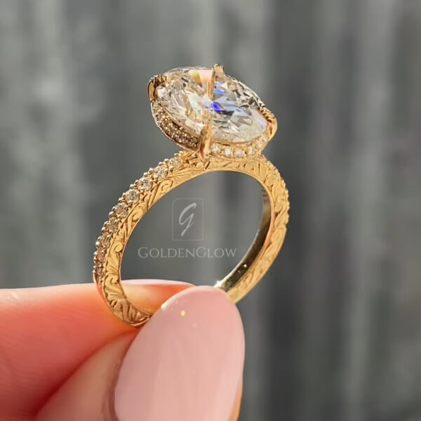A sharp profile view focusing on the prong setting. The yellow gold claws are refined and unobtrusive, letting the oval lab grown diamond or Moissanite dominate. The light passes through the stone's pavilion, illuminating the internal facets. The side engraving on the band adds texture and visual interest. This image showcases the stone's cut quality and the precise engineering of the setting that keeps the large gem secure yet open to light.