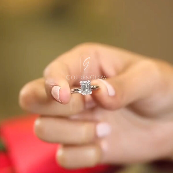 A detailed side profile of a vintage-inspired engagement ring in polished white gold. The band features intricate hand-engraved wheat patterns that add texture and heirloom charm. The center stone, a unique elongated hexagonal step-cut lab grown diamond or Moissanite, is held by claw prongs in a high basket setting. This view emphasizes the elevation of the stone and the craftsmanship of the engraving, making it a perfect choice for a bride seeking Art Deco elegance with modern ethics.