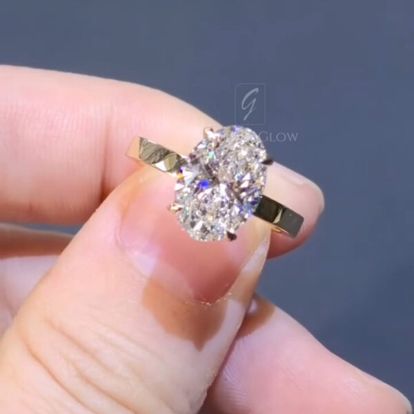 Front-facing close-up of an oval diamond solitaire ring highlighting the symmetry and brilliance of the center stone. The yellow gold band frames the diamond with a warm contrast, while the prongs subtly rise around the oval shape. Light dispersion across the facets creates flashes of sparkle. The overall look is classic, refined, and elegant, emphasizing a timeless engagement ring aesthetic.